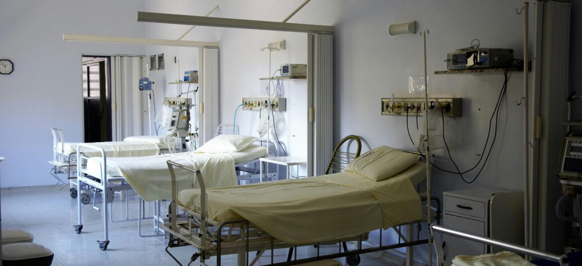 Spacious hospital room with several empty beds and medical equipment, emphasizing healthcare and hygiene.